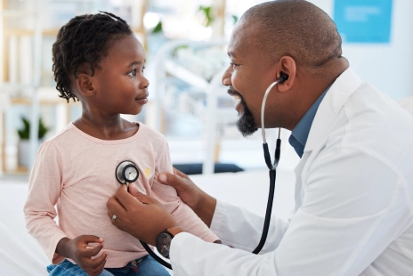 A doctor holds a stethoscope to a child’s chest.